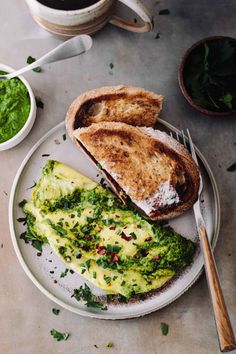 an omelet and toast on a plate next to two cups of green tea