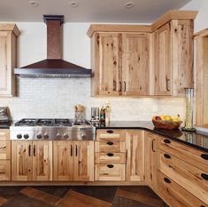 a kitchen with wooden cabinets and black counter tops, an oven hood over the stove