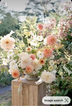 a vase filled with lots of flowers sitting on top of a wooden post in front of some bushes