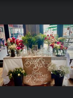 a table topped with lots of vases filled with flowers and greenery next to a sign that says bloom bar