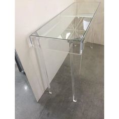 a clear glass table sitting on top of a cement floor next to a white wall