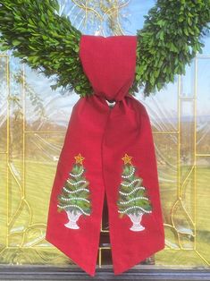 a red scarf with a christmas tree on it and two green wreaths hanging from the front