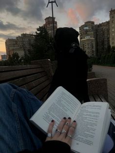 a person is sitting on a bench with an open book in their lap and the sun setting behind them