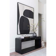 a black and white painting hangs on the wall above a console table with vases