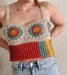 a woman wearing a crocheted top with flowers on the front and sides, standing against a white wall