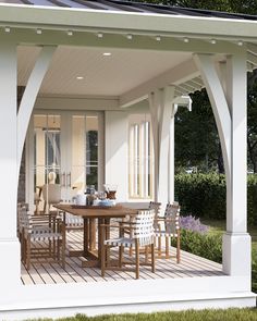 an outdoor dining area with table and chairs on wooden decking next to white building