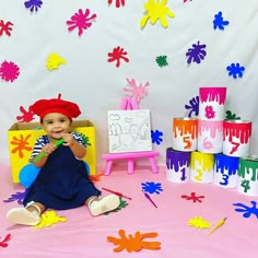 a baby sitting on the ground in front of some paint splatters