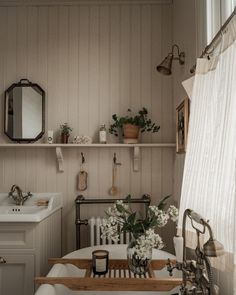 a bath tub sitting next to a sink in a bathroom under a window with white curtains