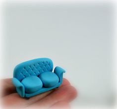 a miniature blue couch sitting on top of a persons hand in front of a white wall