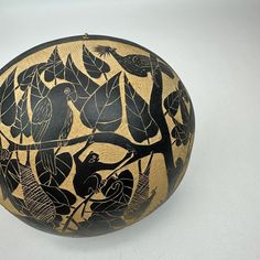 an old black and gold vase with birds on it's side, sitting on a white surface