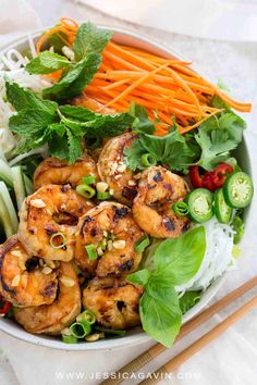 a bowl filled with shrimp, carrots and lettuce next to chopsticks