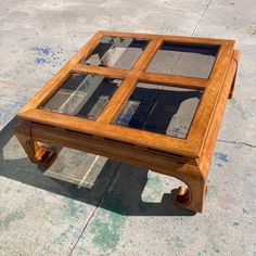 a wooden table with glass top sitting on concrete