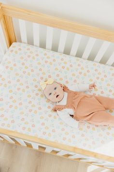 a baby is laying in a crib and looking at the camera while wearing a brown outfit