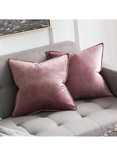 two pink pillows sitting on top of a gray couch