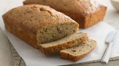 sliced loaf of banana bread sitting on top of a white napkin next to a knife and fork