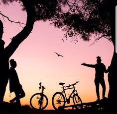 two people standing next to each other with bikes in front of them at sunset or dawn