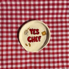 a plate with the words yes chef on it sitting on a red and white checkered table cloth