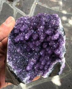 a person holding up a purple rock with lots of crystals on it's surface