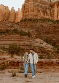 a man and woman standing next to each other in front of some mountains with rocks