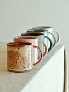 three coffee mugs sitting on top of a table next to each other in different colors