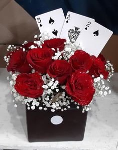 red roses and baby's breath in a black box with playing cards on the table