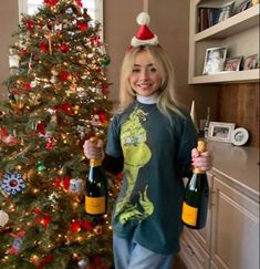 a woman holding two champagne bottles in front of a christmas tree