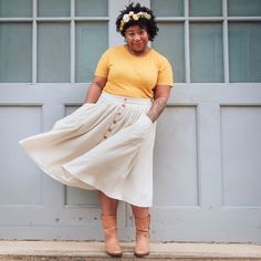 a woman standing in front of a garage door wearing a yellow shirt and white skirt