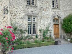 an old stone house with pink flowers in the front yard and large windows on each side