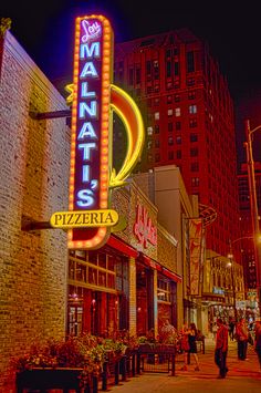 people are walking on the sidewalk in front of a restaurant and pizza shop at night