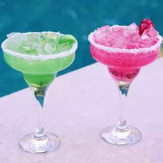 two cocktails sitting next to each other on top of a table near a swimming pool