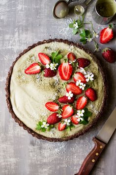 there is a pie with strawberries on it next to a knife and some flowers