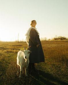 a woman standing next to a goat in a field