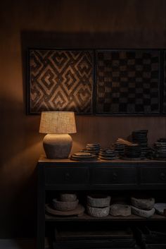 a lamp sitting on top of a wooden table next to bowls and plates in front of a wall