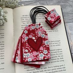 an open book with flowers and hearts on it next to some hair clips in the shape of a heart