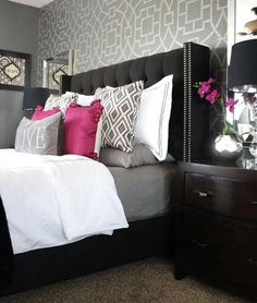 a bedroom with grey and white wallpaper, black headboard, pink pillows, and gray bedding