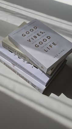 three books stacked on top of each other in front of a white wall with shadows