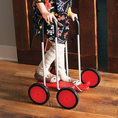 a little boy riding on a red and black hand truck with wheels that are attached to the handlebars