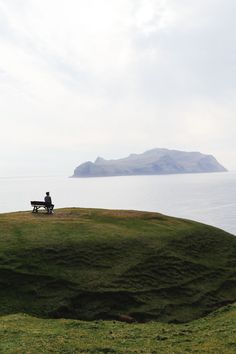 a person sitting on a bench overlooking the water and land with an island in the distance