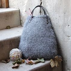 a gray purse sitting on the steps next to a ball of yarn