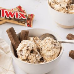 two bowls filled with ice cream and chocolate covered candy bars next to each other on a white surface