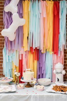 a table topped with cake and desserts next to a colorful wall covered in streamers