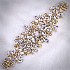 Add a touch of classic elegance to your bridal gown with this sparkling beaded belt! Adorned with an array of glowing crystals on a yellow gold base, it will give your dress an extra touch of glam to finish off your perfect look on your wedding day.The crystal appliqué measures approx. 12" long by 2 1/4" wide. It can be ordered as appliqué only to be sewn onto your dress, or attached to your choice of white or ivory double-faced satin ribbon, 1.5" wide and with a total length of 3 yards (108"). Elegant White Bridal Belt With Bling, Gold Crystal Bridal Belt For Party, Elegant Gold Bridal Belt With Rhinestones, Luxurious Gold Bridal Belt With Embellishments, Luxury Bridal Belt With Crystal Embellishments, Gold Crystal Bridal Belt For Wedding, Luxury Crystal Embellished Bridal Belt, Crystal Embellished Bridal Belt, Fitted Crystal Bridal Belt Embellished