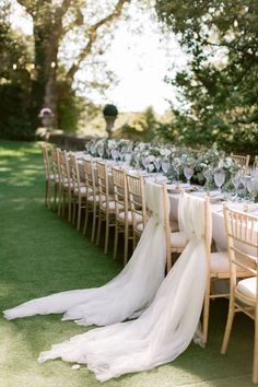 a long table is set up with white linens and chairs for an outdoor wedding