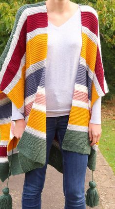 a woman standing on a sidewalk wearing a colorful striped cardigan with tassels