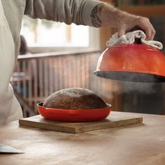 a person is holding a red pot over a loaf of bread on a wooden table