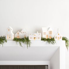 a white mantle with christmas decorations on it and houses in the background, all lit up