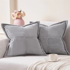 two gray pillows sitting on top of a white couch next to a vase with flowers