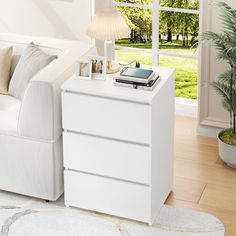 a living room with a white couch and a phone on top of a dresser next to a window