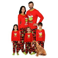 the family is wearing matching red pajamas and posing for a photo with their dog in front of them