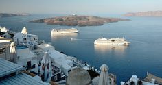 two cruise ships are in the water near some white buildings and sand hills on an island